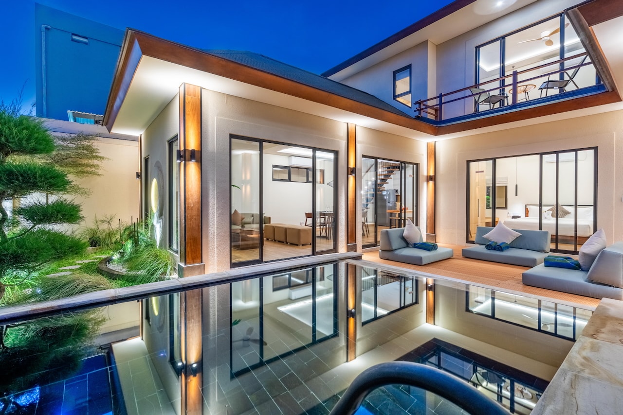 The whole villa at blue hour, every room lit and mirrored in the pool